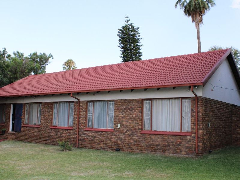 A single-story face brick house featuring a red tiled roof, metal security gates, and established garden surroundings.