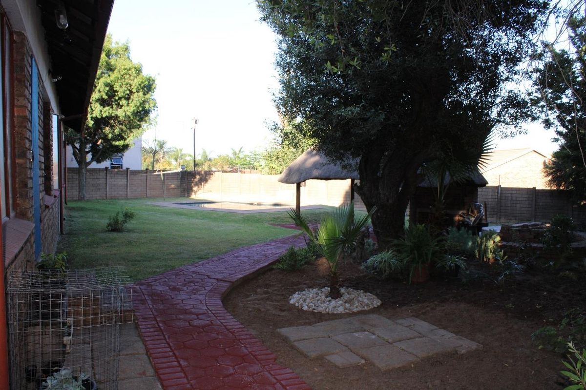 Spacious rear garden featuring a swimming pool, a traditional thatched lapa, and a paved walkway leading through the landscaped yard.