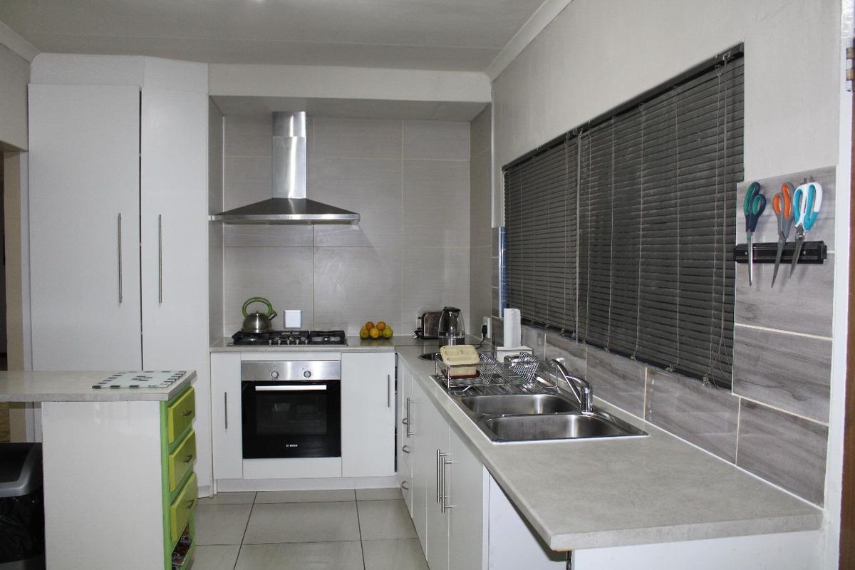 A functional kitchen featuring white cabinetry, a gas hob with extractor fan, electric oven, and a double basin sink with tiled splashbacks.