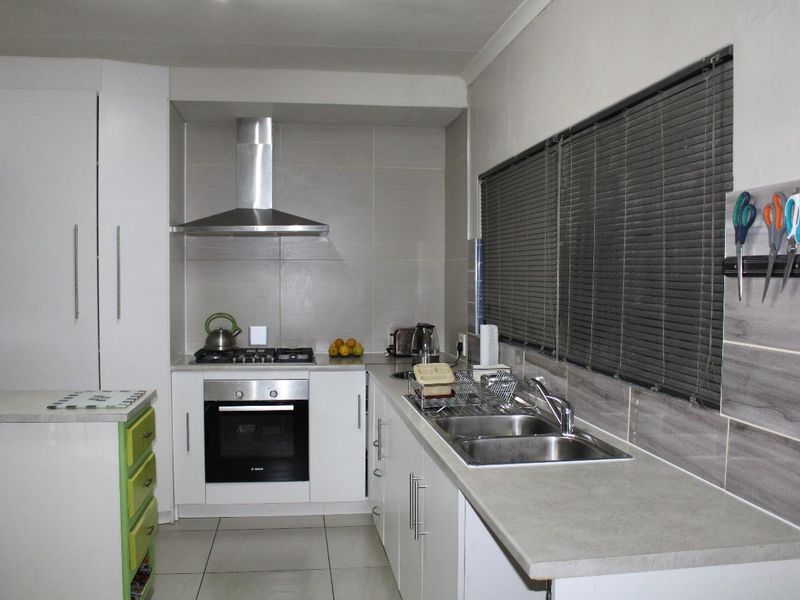 A functional kitchen featuring white cabinetry, a gas hob with extractor fan, electric oven, and a double basin sink with tiled splashbacks.