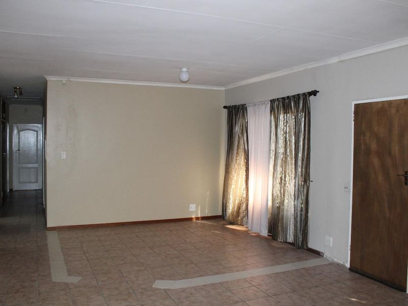 An empty living room featuring tiled flooring, neutral walls, and access to an adjacent hallway, offering a blank canvas for interior design.