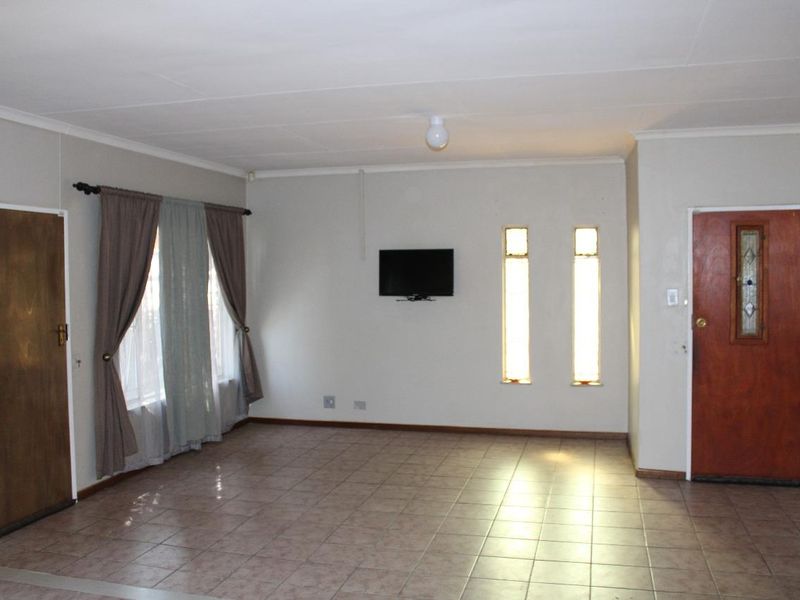 A spacious, neutrally painted living room featuring tiled flooring, vertical accent windows, and a solid timber entrance door.