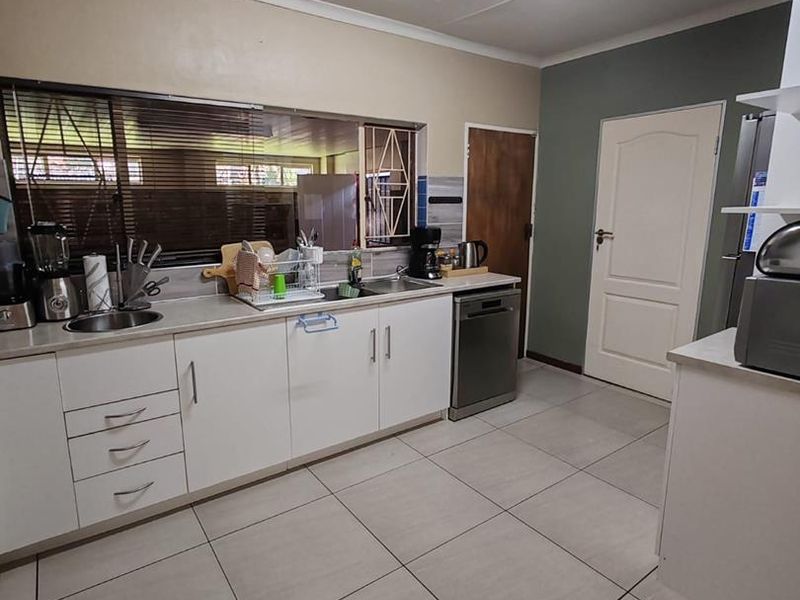 A functional kitchen featuring white cabinetry, laminate countertops, tiled flooring, and a stainless steel sink with integrated dishwasher space.