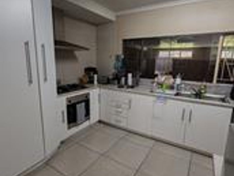 A functional kitchen featuring white built-in cabinetry, a stainless steel sink, integrated oven, gas hob, extractor fan, and neutral tiled flooring.