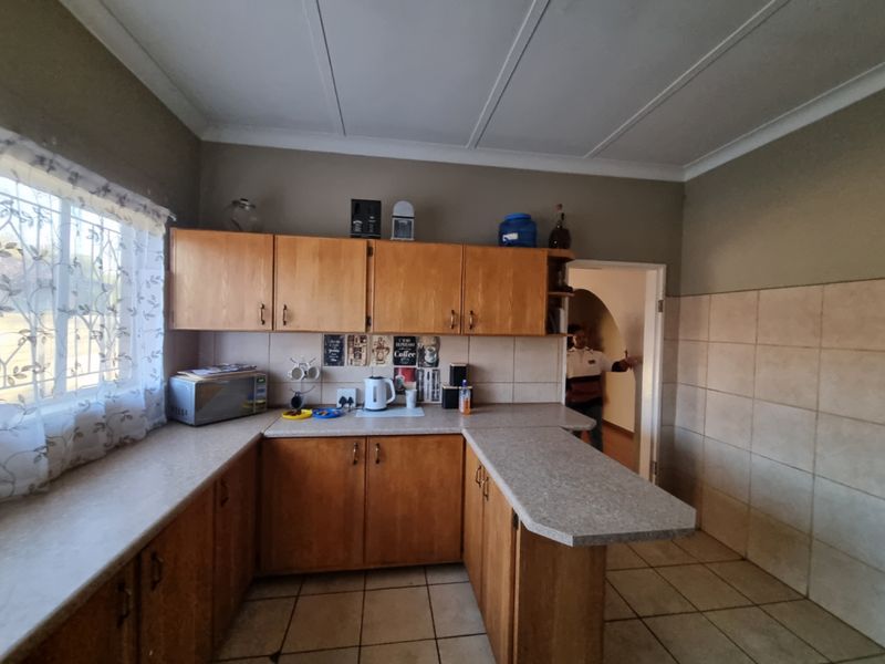 A functional kitchen featuring wooden cabinetry, laminate countertops, and tiled flooring, offering a practical layout with potential for modern updates.