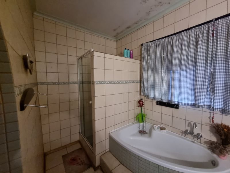 A dated bathroom featuring a built-in bathtub and a separate tiled shower enclosure, requiring cosmetic updates and ceiling repairs.