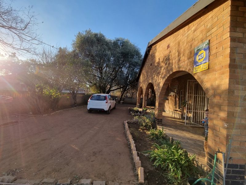 Front exterior view of a brick house featuring an arched veranda, security gate, and a spacious driveway area.