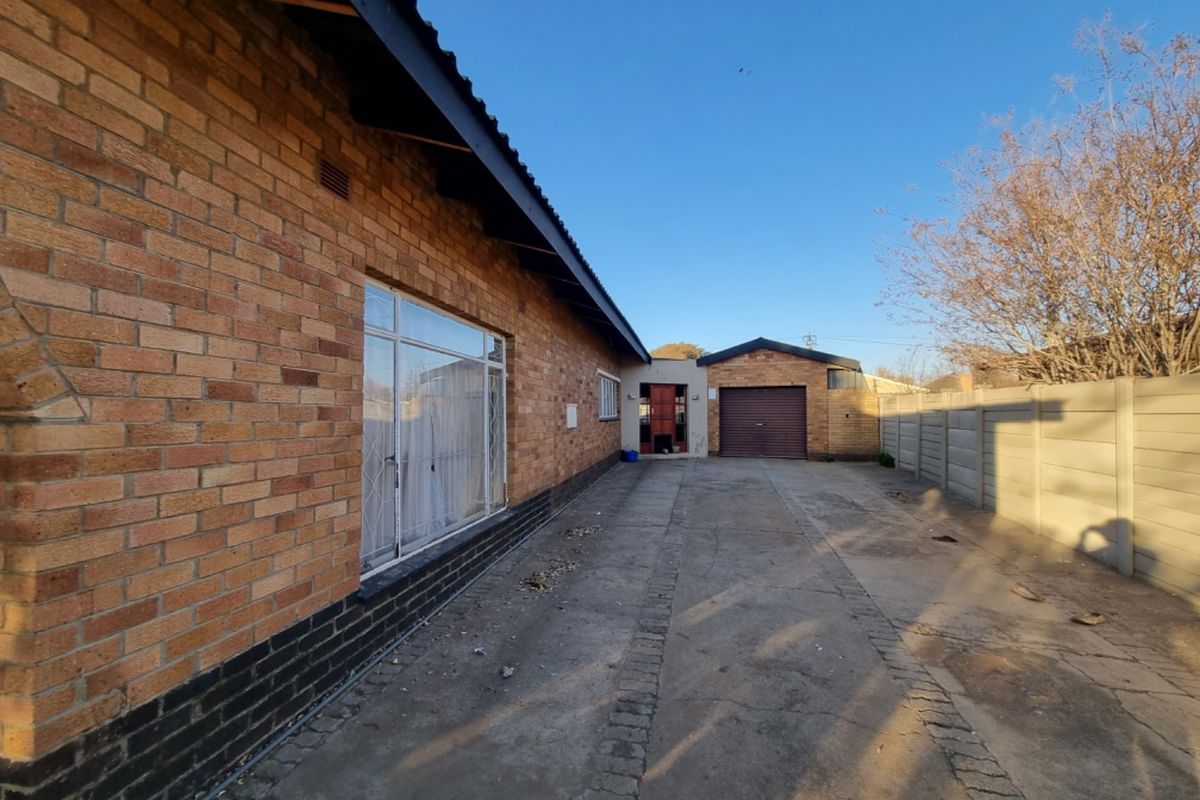 Rear exterior view showing a face brick house facade, concrete driveway, and a detached garage with a precast boundary wall.