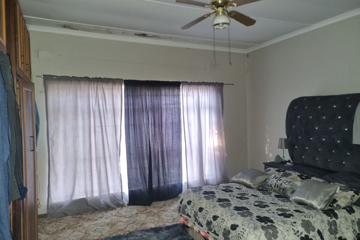 Spacious bedroom featuring built-in cupboards and a ceiling fan, requiring maintenance to address visible ceiling water damage and wall finish deterioration.