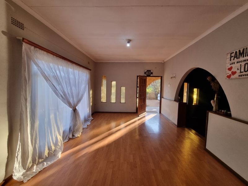 A spacious, sunlit living area featuring laminate flooring, a distinctive arched entryway, and vertical accent windows, offering a blank canvas for interior design.