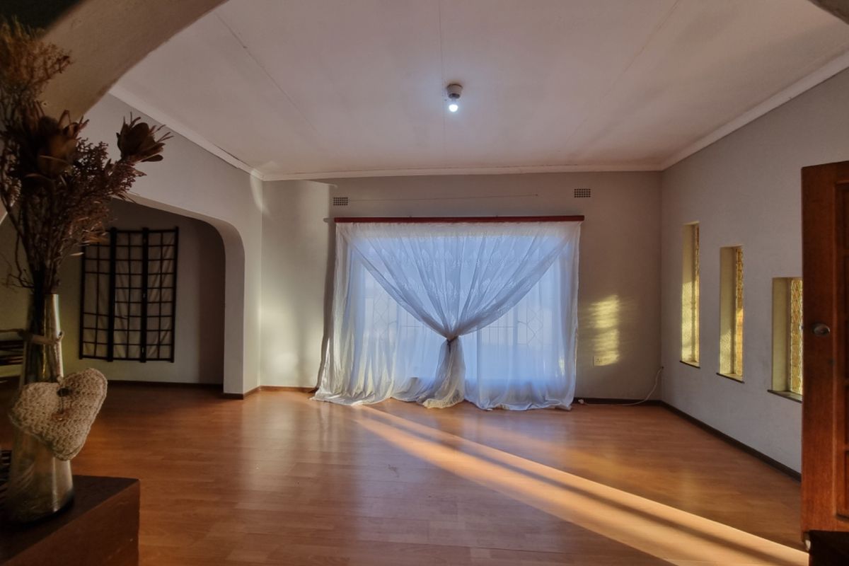 A spacious, empty living room featuring laminate flooring, an architectural archway, and natural light streaming through large windows with sheer curtains.
