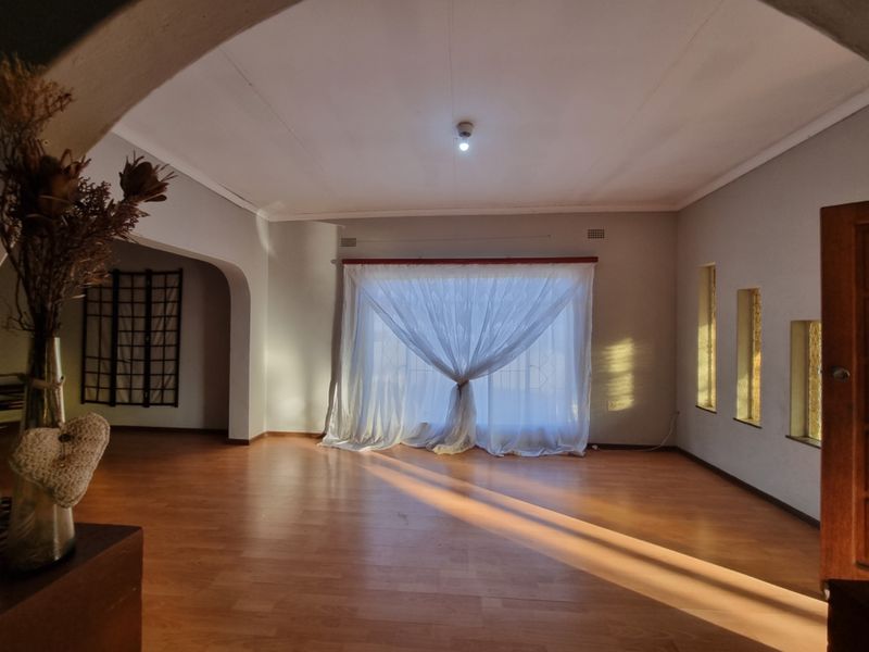 A spacious, empty living room featuring laminate flooring, an architectural archway, and natural light streaming through large windows with sheer curtains.