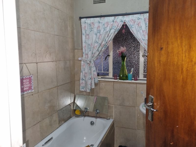 A compact bathroom featuring a bathtub, tiled walls, and a window with security bars, requiring some cosmetic updates to improve its overall condition.