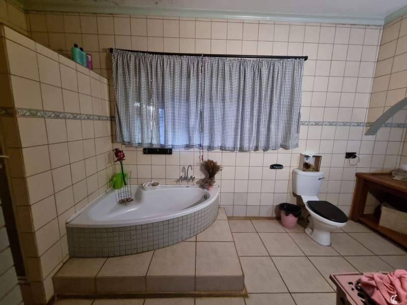 A dated bathroom featuring a corner bathtub, tiled walls and flooring, and a toilet, offering potential for a modern renovation.