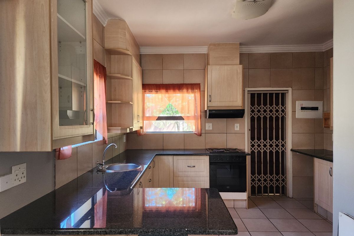 Functional kitchen featuring granite countertops, built-in oven with gas hob, extractor fan, and ample cabinetry, finished with neutral wall and floor tiling.