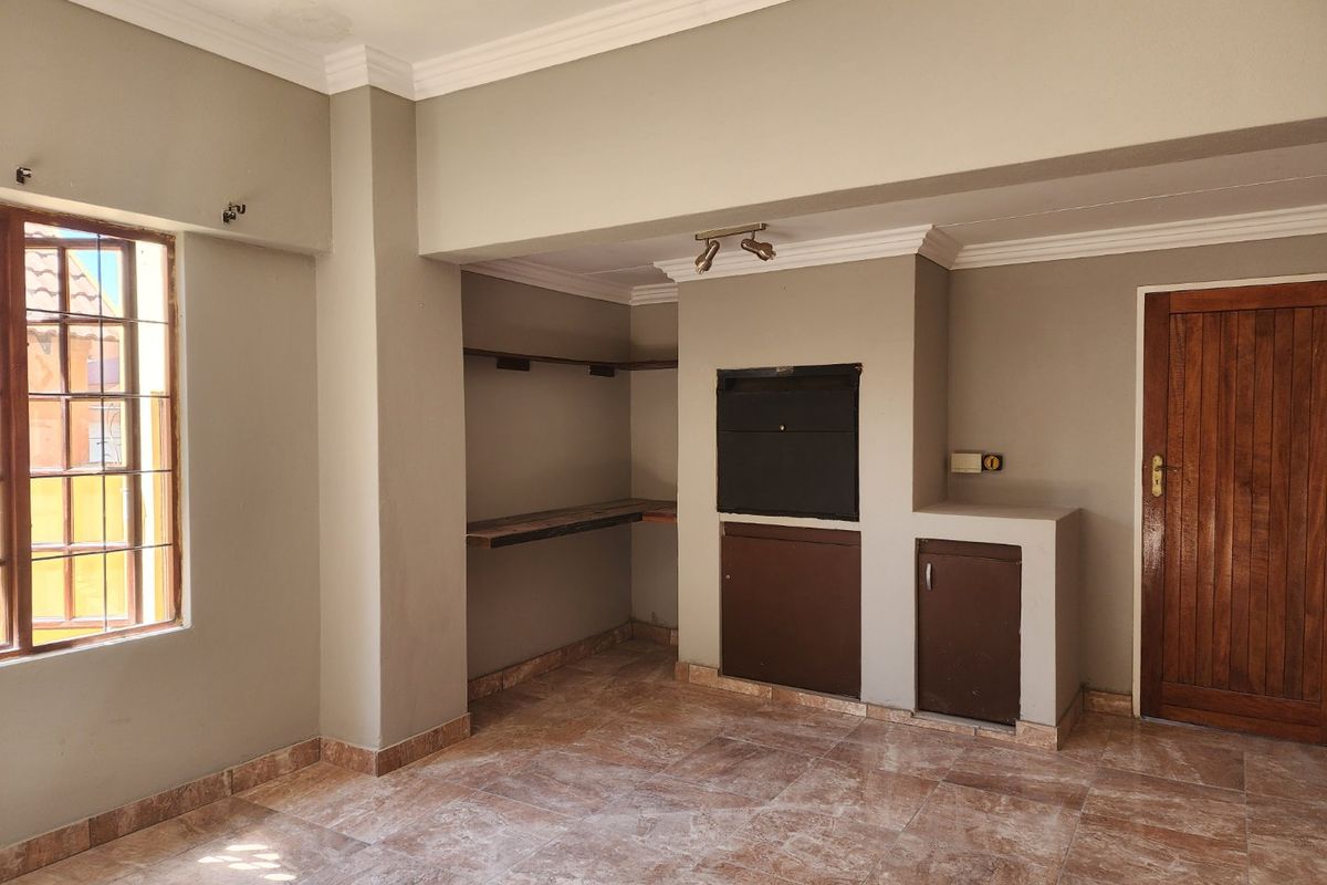 An empty living area featuring tiled flooring, crown molding, and a built-in fireplace with adjacent storage cabinetry.
