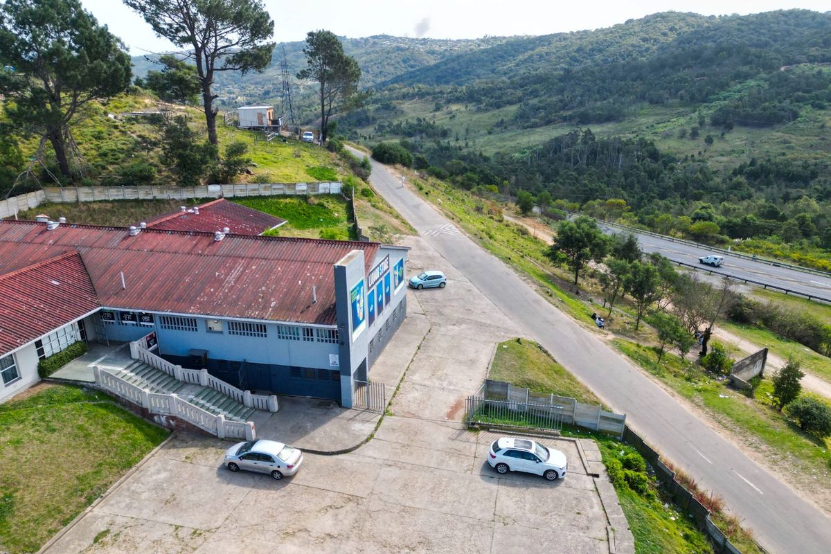 Aerial view of a commercial property featuring a large building with a metal roof, paved parking area, and direct access to the adjacent road.
