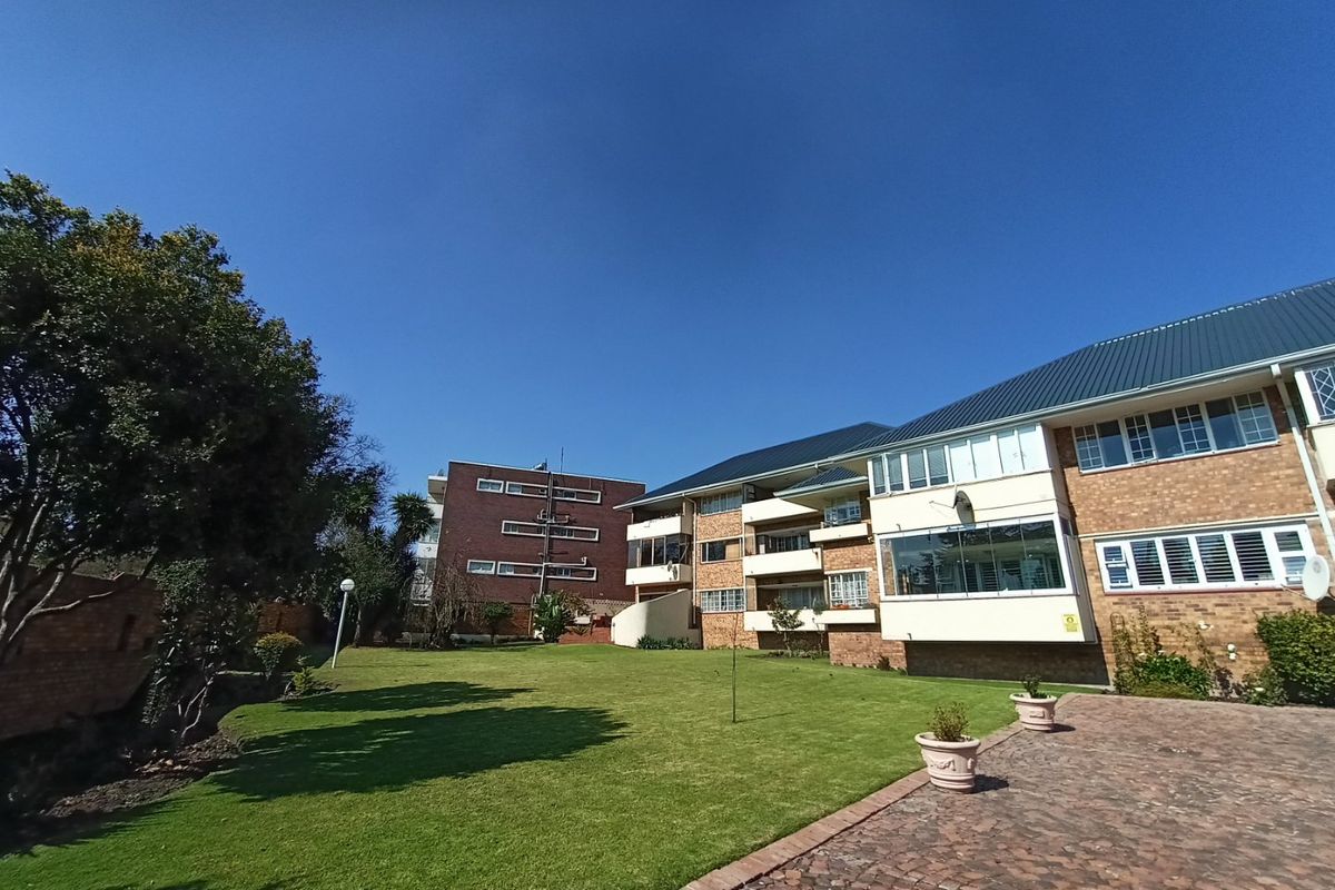 Rear view of a multi-story apartment complex featuring brick facades, pitched metal roofing, private balconies, and a well-maintained communal lawn area.