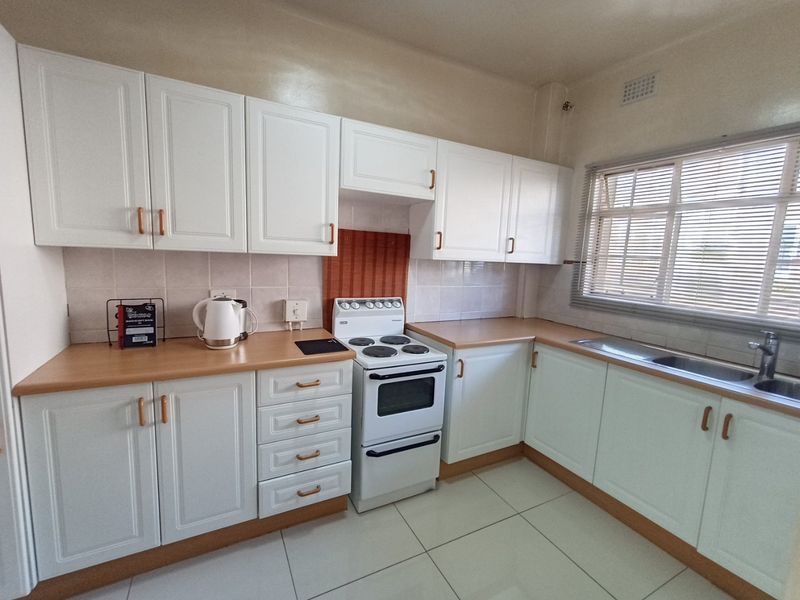 A clean and functional kitchen featuring white cabinetry, laminate countertops, a tiled backsplash, and a freestanding stove with a double oven.