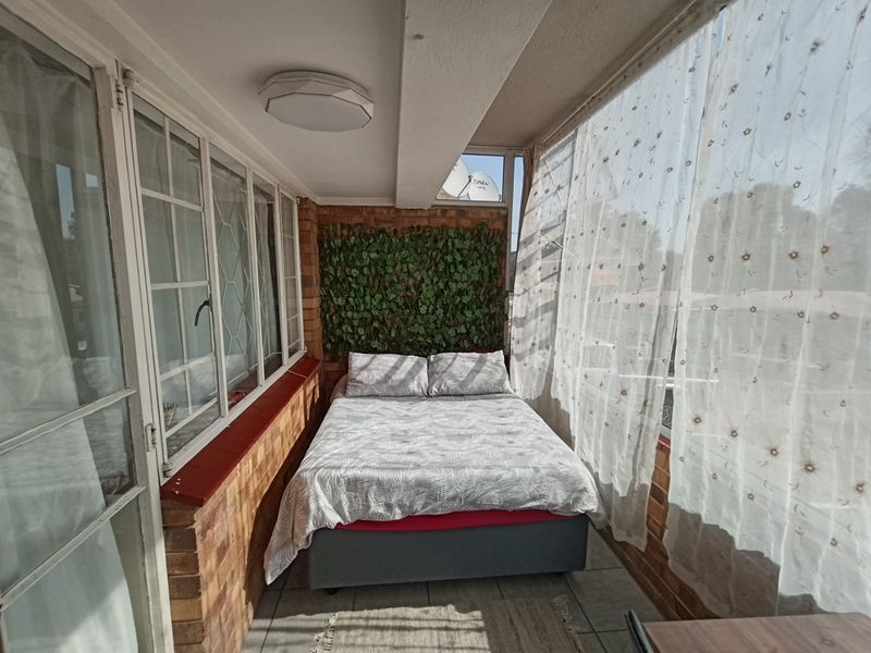 An enclosed balcony space featuring tiled flooring and exposed brick walls, currently utilized as a sleeping area.