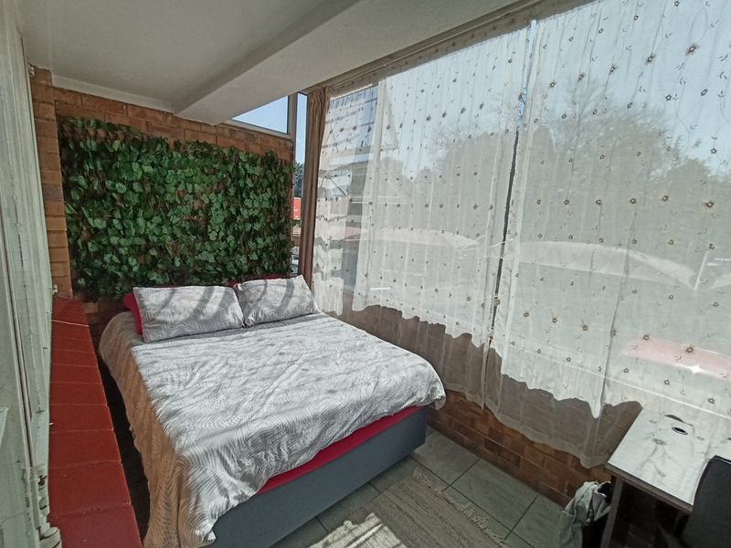 A bedroom featuring exposed brick walls, tiled flooring, and a large window allowing for natural light.