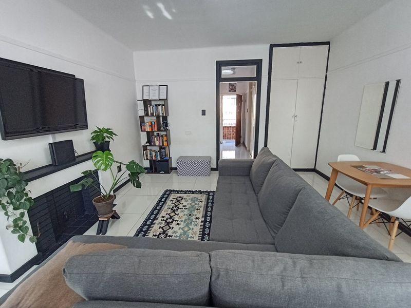A bright living room featuring tiled flooring, a built-in fireplace, and a tall built-in storage cupboard, offering a clean and functional living space.