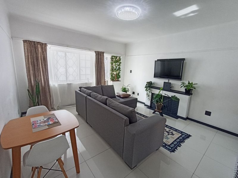 A bright and well-maintained living room featuring tiled flooring, a central fireplace, and large windows with security bars, offering a clean and functional space.