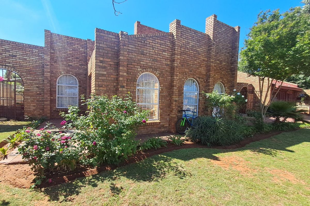 A well-maintained face brick rear facade featuring arched windows, a paved patio area, and a lush, established garden.