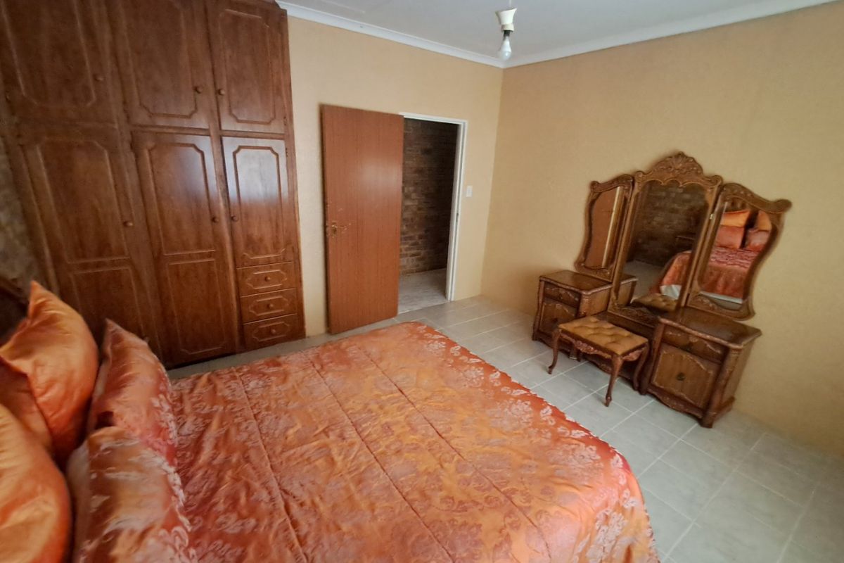 A bedroom featuring tiled flooring and a large built-in wooden wardrobe, offering functional storage space.