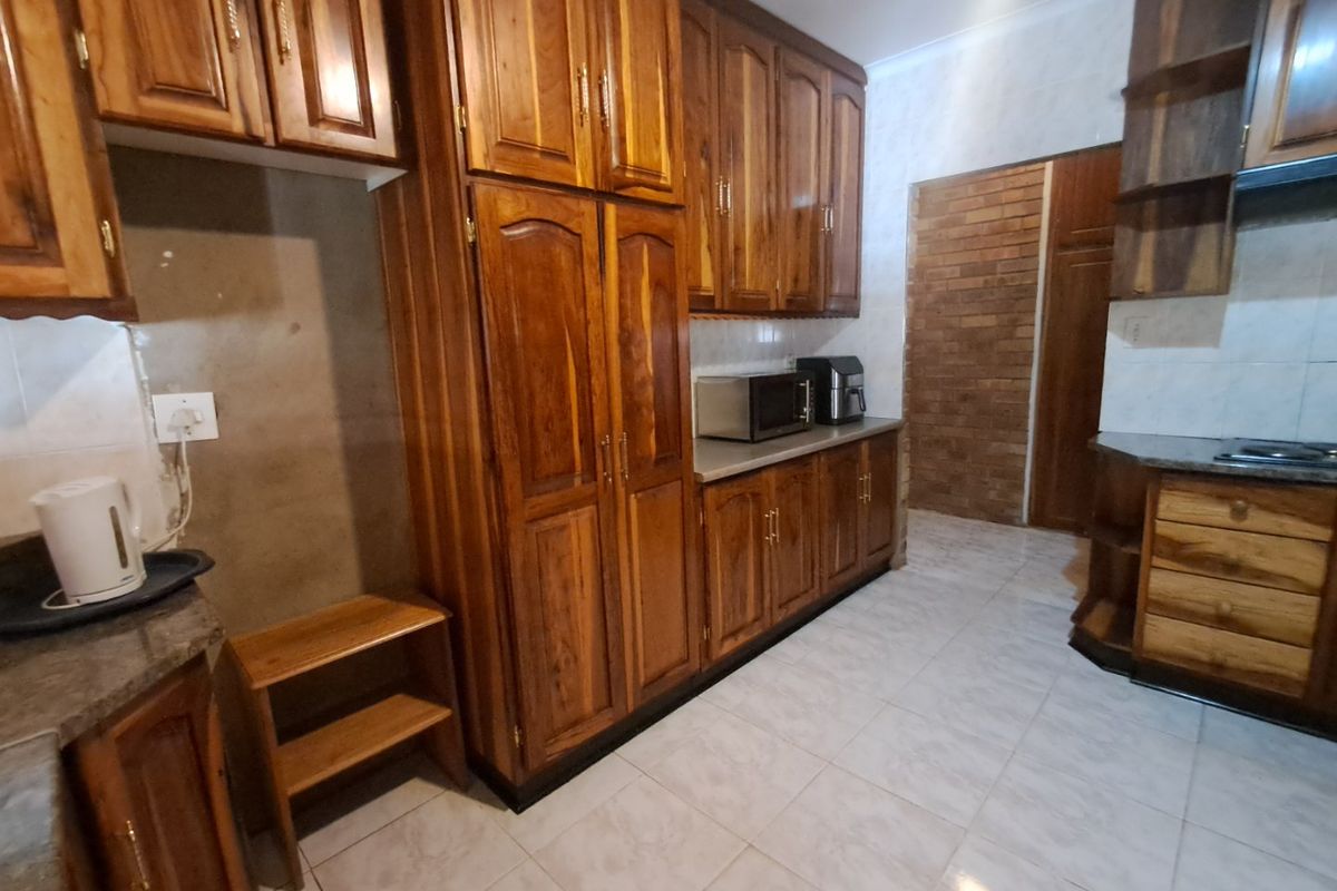 A kitchen featuring traditional wooden cabinetry, stone countertops, tiled flooring, and a distinctive exposed brick wall section.
