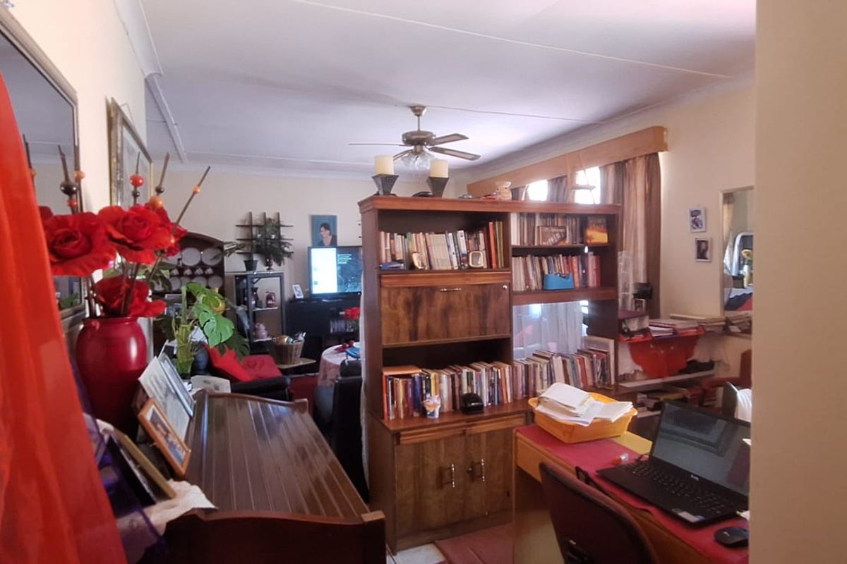 A living room area featuring a ceiling fan and coving, currently furnished with various personal items and storage units.