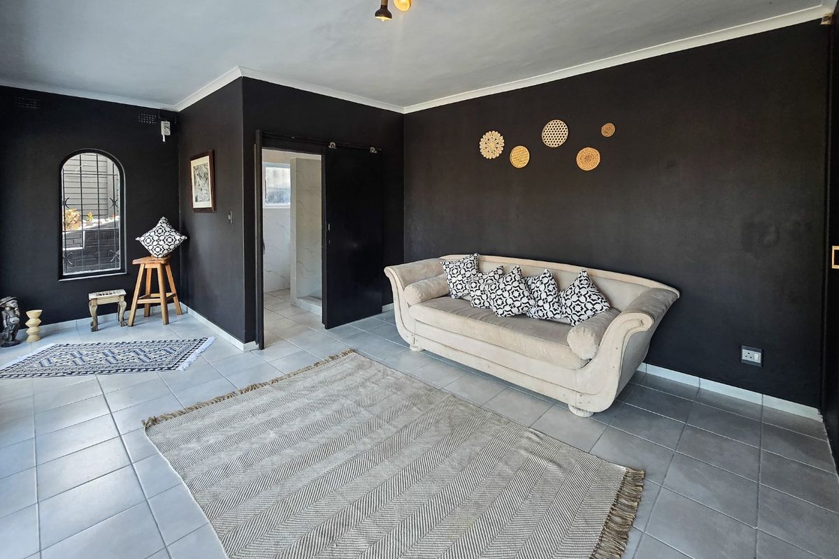 A living room featuring dark painted walls, tiled flooring, an arched window, and a doorway leading to an adjacent space.