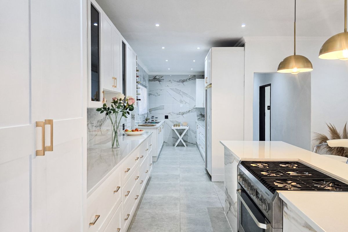 Modern, high-end kitchen featuring white cabinetry, marble-look countertops and backsplash, gas stove, and elegant pendant lighting in a clean, contemporary layout.