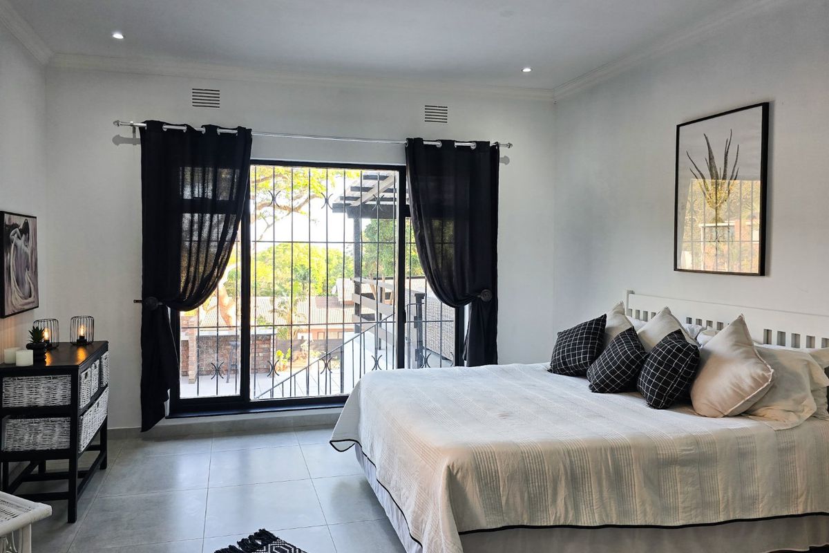 A bright and well-maintained bedroom featuring neutral tiled flooring, recessed lighting, and a sliding glass door providing access to an outdoor balcony area.