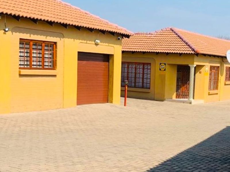 Exterior view of a townhouse complex featuring a paved driveway, multiple garage doors, and tiled roofing.
