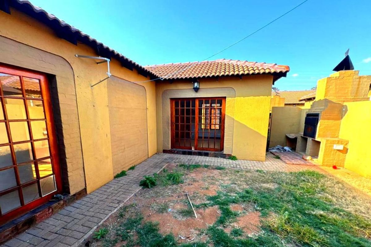 Rear exterior area featuring a built-in braai, paved walkway, and wooden sliding doors leading into the townhouse.