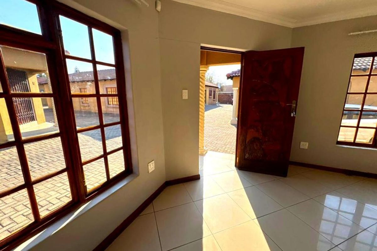 An empty living area featuring tiled flooring, wooden window frames, and direct access to an exterior paved courtyard.