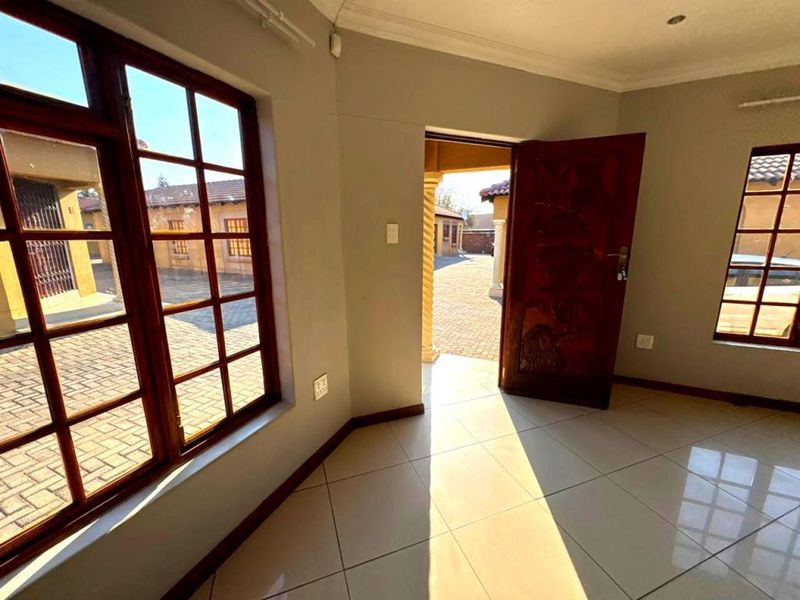 An empty living area featuring tiled flooring, wooden window frames, and direct access to an exterior paved courtyard.