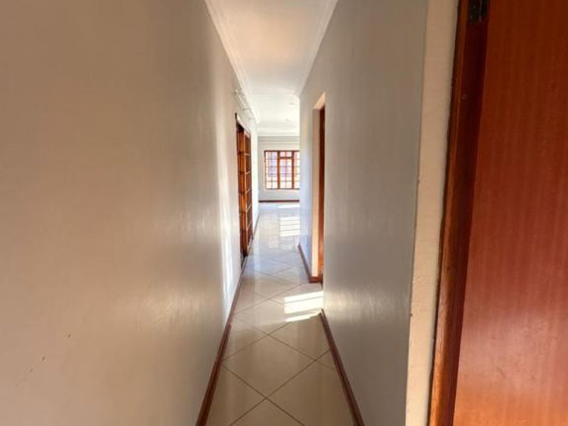 A clean, well-lit hallway featuring neutral wall tones, tiled flooring, and wooden door frames leading to adjacent rooms.