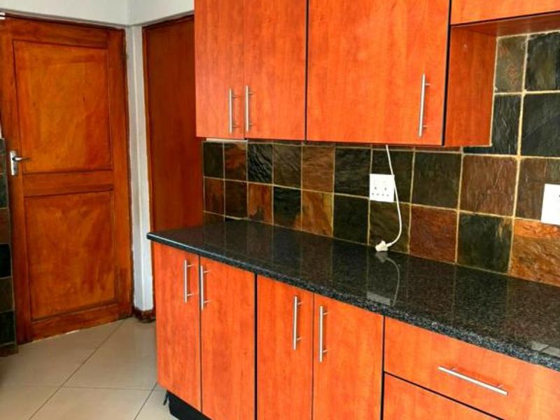 A functional kitchen featuring granite countertops, wood-finish cabinetry, and a slate tile backsplash with ceramic floor tiles.