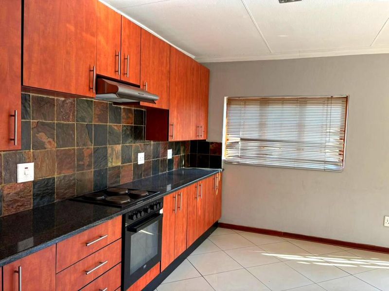A functional kitchen featuring wood-finish cabinetry, dark stone countertops, a built-in oven with hob, and a slate tile backsplash.
