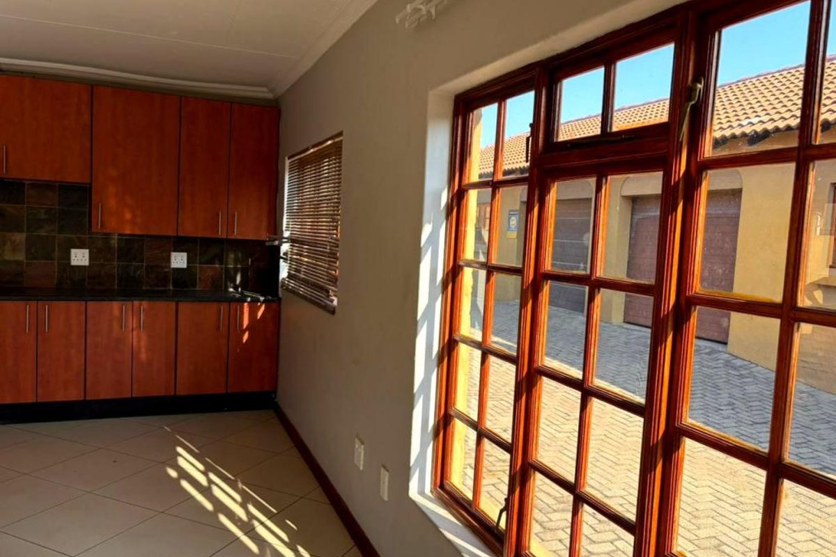 A functional kitchen area featuring wooden cabinetry, tiled backsplash, and large wooden-framed windows overlooking the exterior driveway.