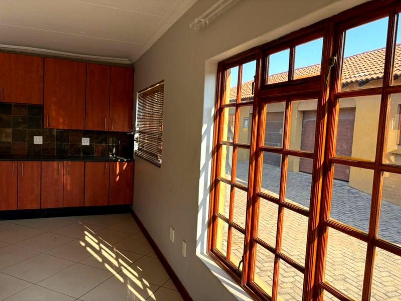 A functional kitchen area featuring wooden cabinetry, tiled backsplash, and large wooden-framed windows overlooking the exterior driveway.