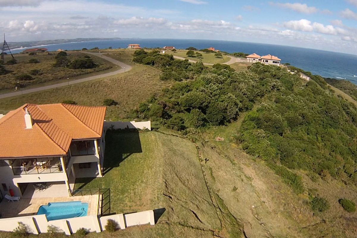 Aerial view of a residential property featuring a swimming pool, patio, and tiled roof, situated in a coastal estate setting.
