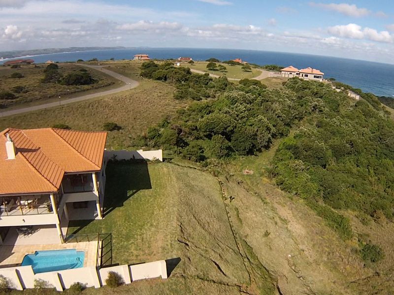 Aerial view of a residential property featuring a swimming pool, patio, and tiled roof, situated in a coastal estate setting.