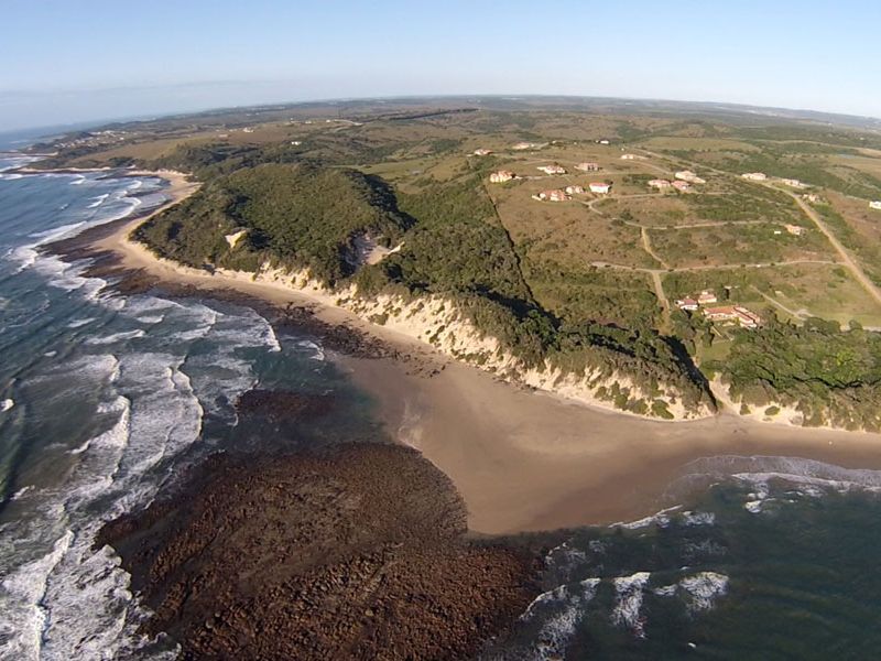 An aerial view of the coastal landscape, showcasing the beach, rocky shoreline, and surrounding natural terrain.