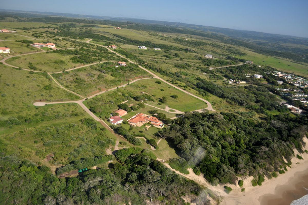 An aerial view of a residential estate featuring expansive green landscapes, paved road infrastructure, and proximity to the coastline.
