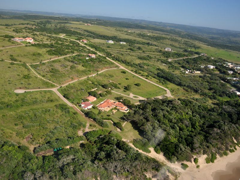 An aerial view of a residential estate featuring expansive green landscapes, paved road infrastructure, and proximity to the coastline.