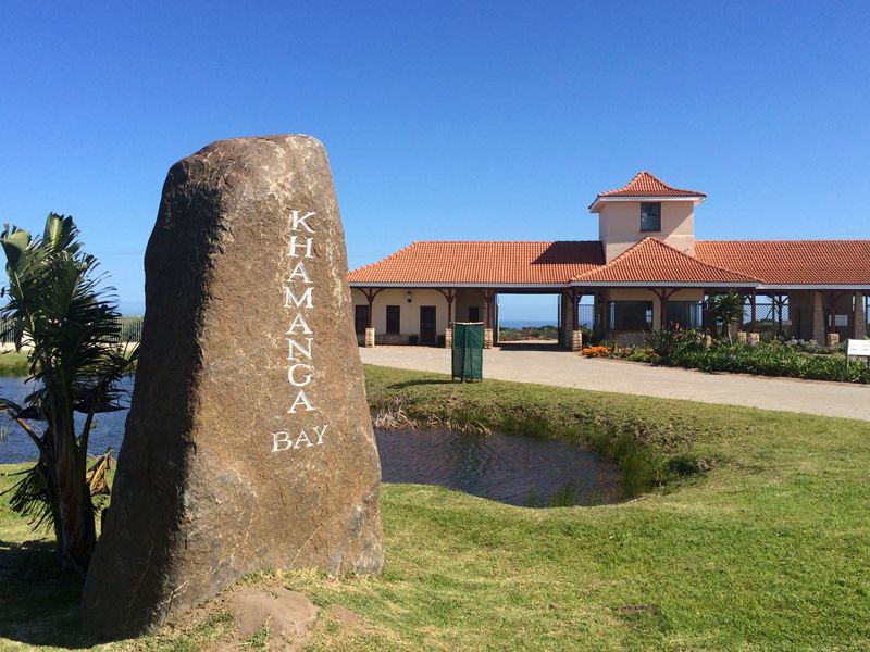 Entrance view of Khamanga Bay estate featuring a prominent stone sign, landscaped grounds, a small water feature, and the main gatehouse structure.