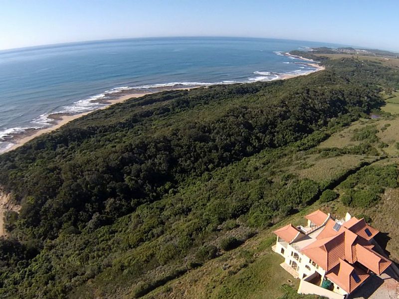 Aerial view of a coastal residential property featuring a multi-level home with a tiled roof and solar panels, overlooking the ocean and forest.